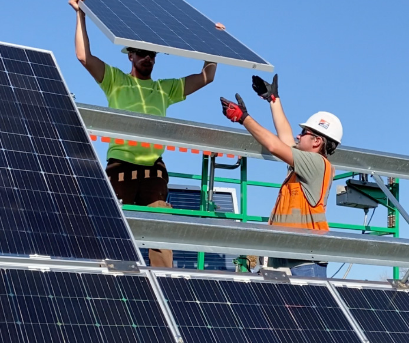 Two men in high visibility clothes install a solar panel on to an array