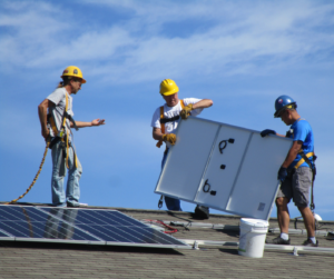 Three workers install a solar panel onto a rooftop array