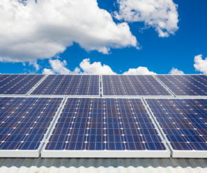A solar array on a metal roof under a blue sky with large, puffy clouds